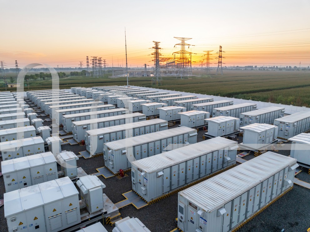 Batteriespeicherpark mit weißen Containern und Strommasten im Hintergrund bei Sonnenuntergang.