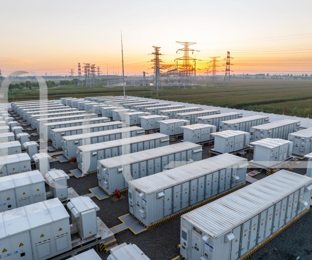 Batteriespeicherpark mit weißen Containern und Strommasten im Hintergrund bei Sonnenuntergang.